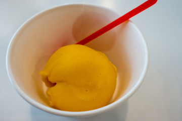 A scoop of Passion fruit ice cream in white paper cup