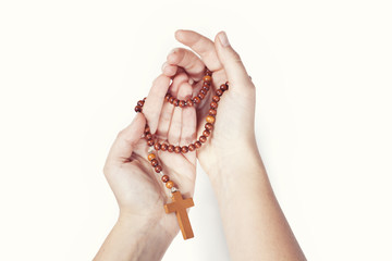 Brown rosary entwined around two female hands on a white background