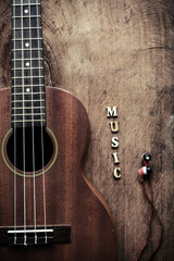 Close up of ukulele and earphone on old wood background