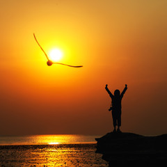Silhouette of traveller with hands raised to birds flying in to