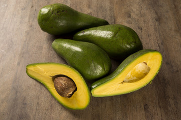 Two whole avocados and a avocado cut in a half over a white surf