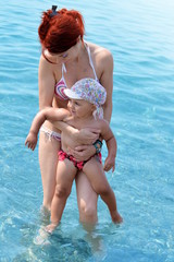 mother teaching baby swimming in tropical sea near beach