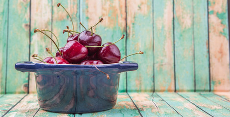 Cherry fruit in a blue pot over weathered light green wooden background