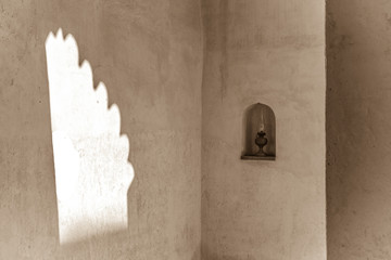 A replica oil lamp sits in an alcove in the entrance to the restored Isa bin Ali house, Muharraq, Bahrain while sunlight streams through the archway onto the wall opposite.