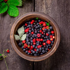 Bowl with wild berries on dark wooden background.