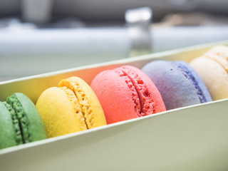 Sweet  pink  french macarons or macaroons between  colorful macarons  in row of box, near a windows.