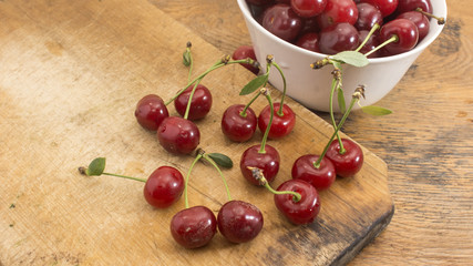 Cherries on wooden chopping board and in white bowl.