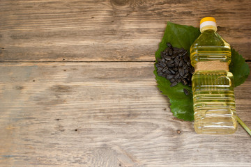 Bottle of sunflower oil and sunflower seeds on wooden background. Copy space to right.