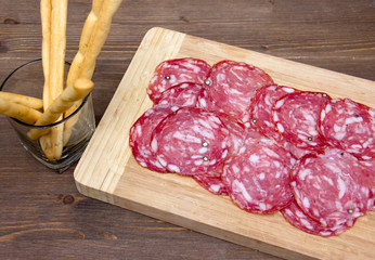 Slices of salami on cutting board and bread sticks on wooden table