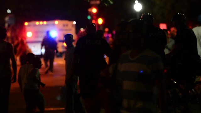 Throngs of people at night with an ambulance
