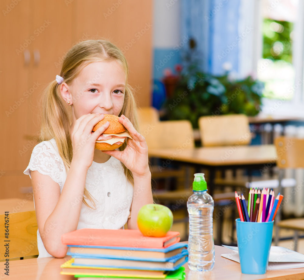 Wall mural schoolgirl looking at camera while having lunch during break