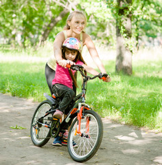 happy mother teaches his daughter to ride a bike