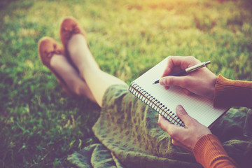 female hands with pen writing on notebook on grass outside - 86479136