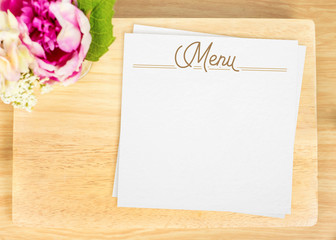Top view of Blank wooden plate with white menu card and flower p