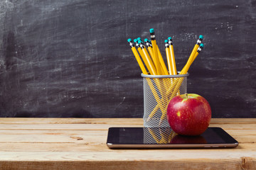Back to school background with tablet, pencils and apple over chalkboard