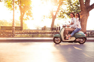 Cheerful young couple riding a scooter and having fun. Sun is shining in the morning