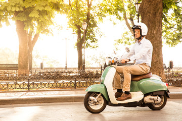 Trendy man driving a scooter in helmet. Sun is shining through trees on background © Drobot Dean