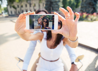 Happy couple showing smartphone screen while making selfie  outdoors