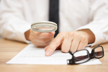 Focused businessman is reading through  magnifying glass documen