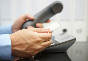 businessman looks on business card for information to make a cal