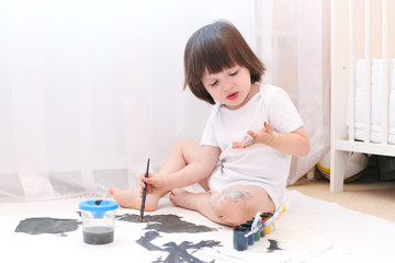 Cute child looks at dirty hands bedaubing with gouache