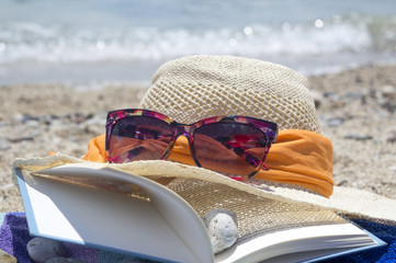 Straw hat sunglasses and a book on the beach with sea in backgou