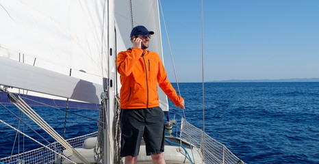 Man sailing with sails out on a sunny day and talking on the phone