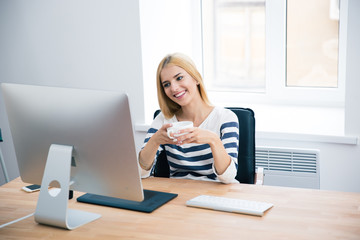 Happy female designer drinking coffee in office