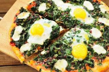 Round green pizza with eggs and mozarella on wooden board