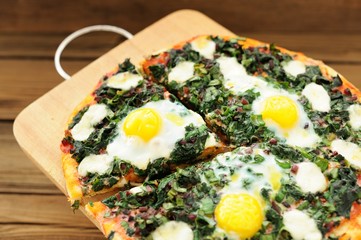 Round green pizza with eggs and mozarella on wooden board