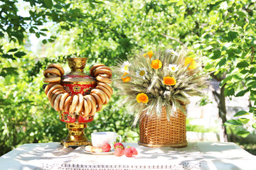 A cup of morning tea on table with samovar and beautiful bouquet of summer flowers on nature background
