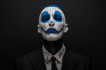 Terrible clown and Halloween theme: Crazy blue clown in black suit isolated on a dark background in...