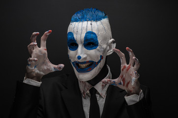 Terrible clown and Halloween theme: Crazy blue clown in black suit isolated on a dark background in the studio