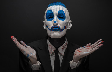 Terrible clown and Halloween theme: Crazy blue clown in black suit isolated on a dark background in...