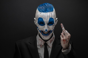 Terrible clown and Halloween theme: Crazy blue clown in black suit isolated on a dark background in the studio