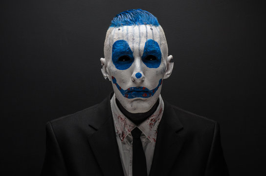 Terrible clown and Halloween theme: Crazy blue clown in black suit isolated on a dark background in the studio