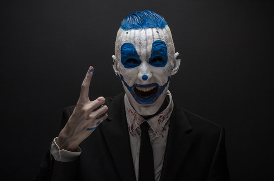 Terrible clown and Halloween theme: Crazy blue clown in black suit isolated on a dark background in the studio