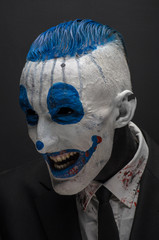 Terrible clown and Halloween theme: Crazy blue clown in black suit isolated on a dark background in the studio