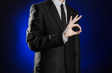 Obraz na płótnie Canvas Business and the presentation of the theme: man in a black suit showing hand gestures on a dark blue background in studio isolated