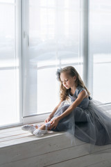 A little adorable young ballerina sitting on window