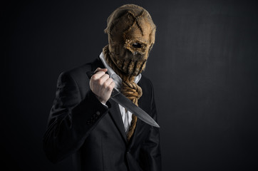 Fear and Halloween theme: a brutal killer in a mask holding a knife on a dark background in the studio