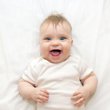 Smiling baby lying on a white bed.