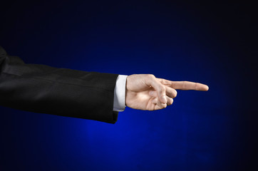 Businessman and gesture topic: a man in a black suit and white shirt showing hand gesture on an isolated dark blue background in studio