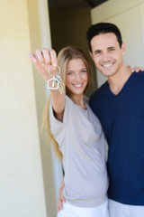 happy young couple man and woman handing over their new home keys in front of open house door