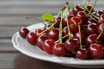 red cherry on the elegant plate standing on wooden background.