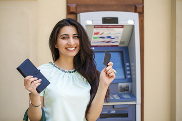 Young woman in jeans short using an automated teller machine