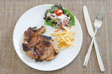 Grilled pork steak with french fries and vegetables on plate