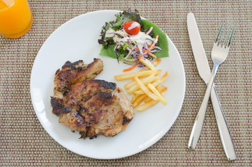 Grilled pork steak with french fries and vegetables on plate