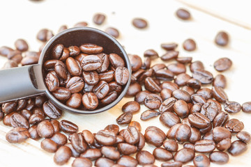 selective focus of coffee beans in spoon  on plank of wooden ,blurred background