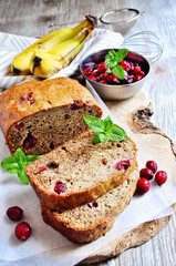 Banana bread loaf with ripe bananas and frozen cranberries on rustic background, selective focus